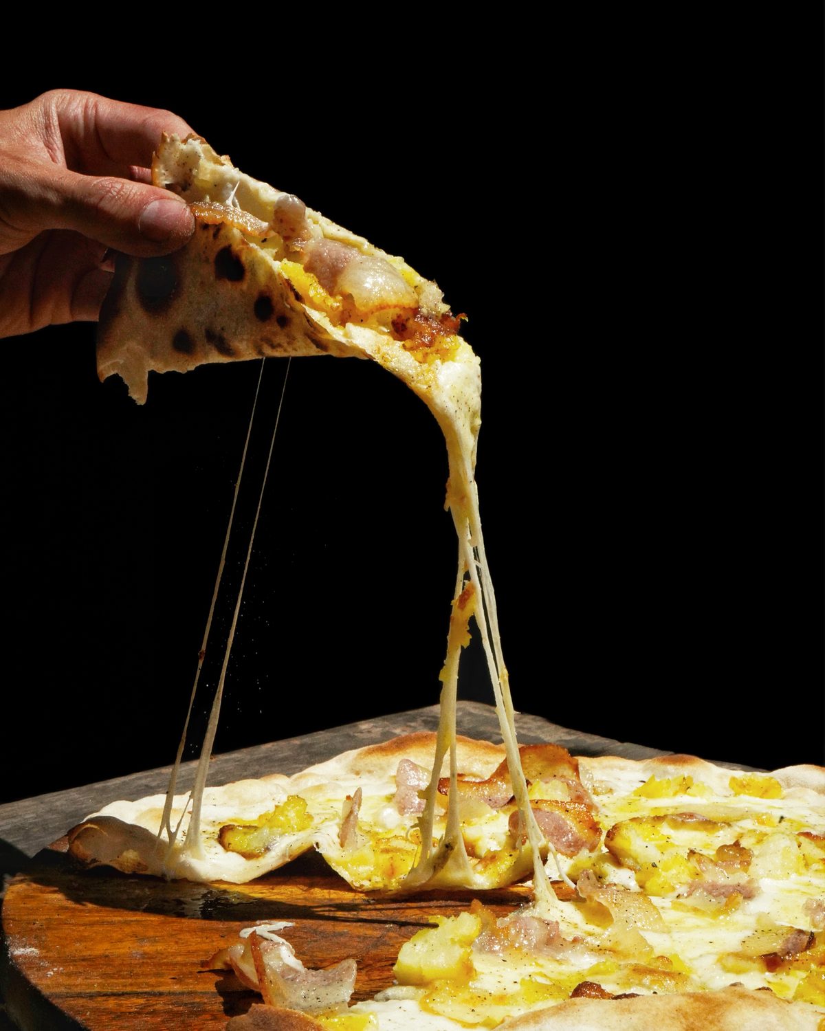 Una fetta di pizza sollevata dalla teglia, la mozzarella che fila